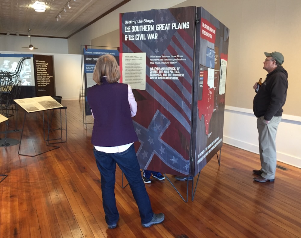 Textured paint over cedar wood and steel exhibit structures with visitors at Chisholm Trail exhibit